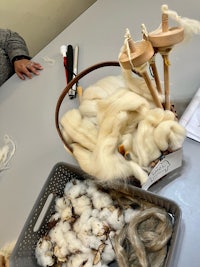 a woman is sitting at a table with a basket of wool